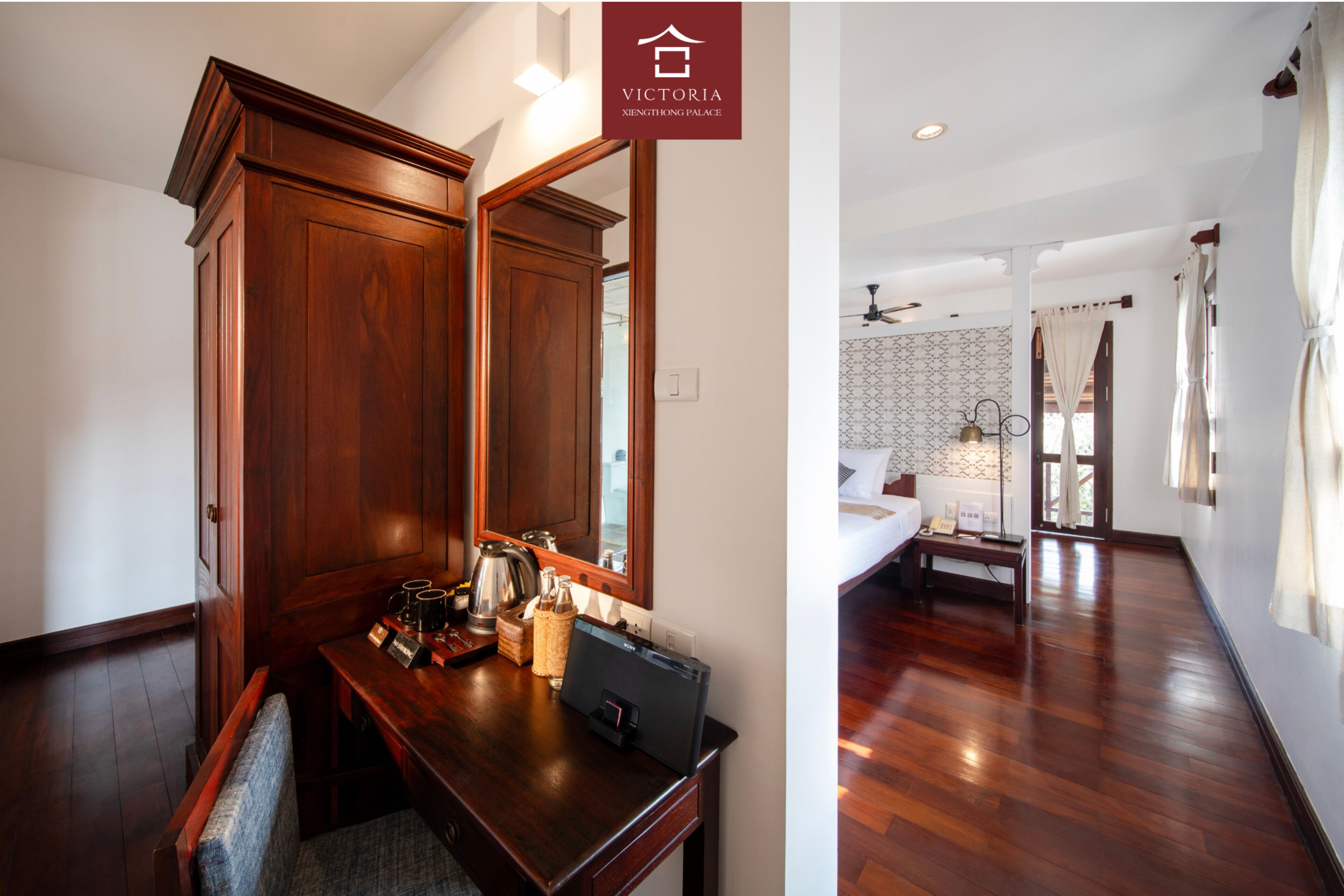 A hotel room with a wooden desk, a mirror, a bed with a nightstand, and a patterned wall.