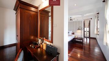 A hotel room with a wooden desk, a mirror, a bed with a nightstand, and a patterned wall.