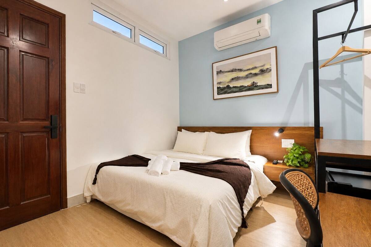 A bedroom with a bed, a desk, a chair, a window, and an air conditioning unit.
