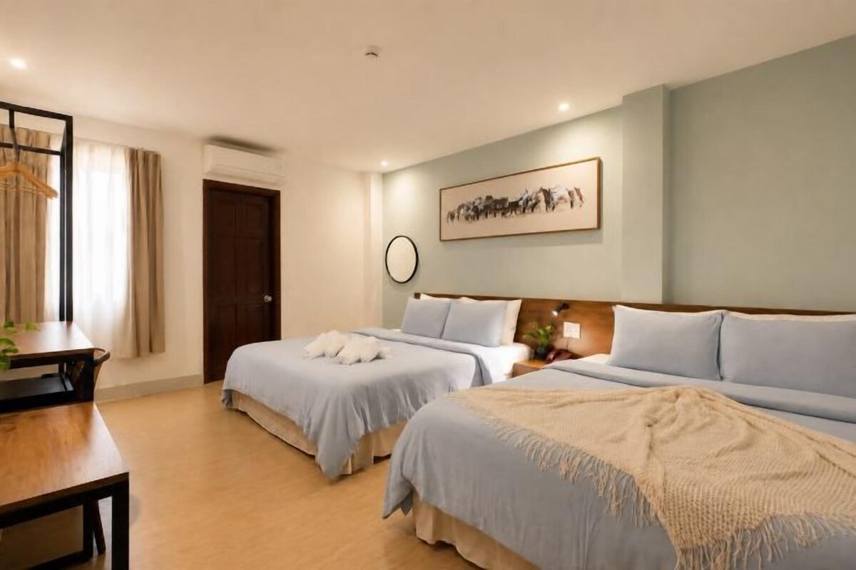 A hotel room with two beds, a desk, a chair, a framed picture on the wall, and a door.