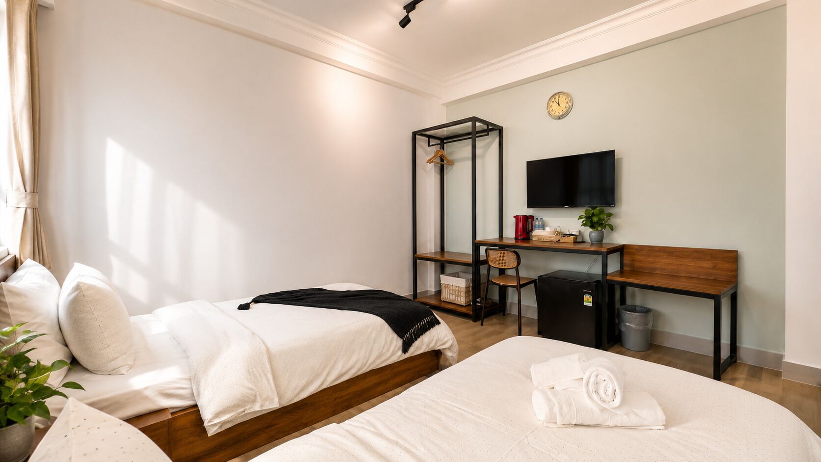 Habitación de hotel con dos camas, un escritorio con televisor, un refrigerador pequeño y una planta.