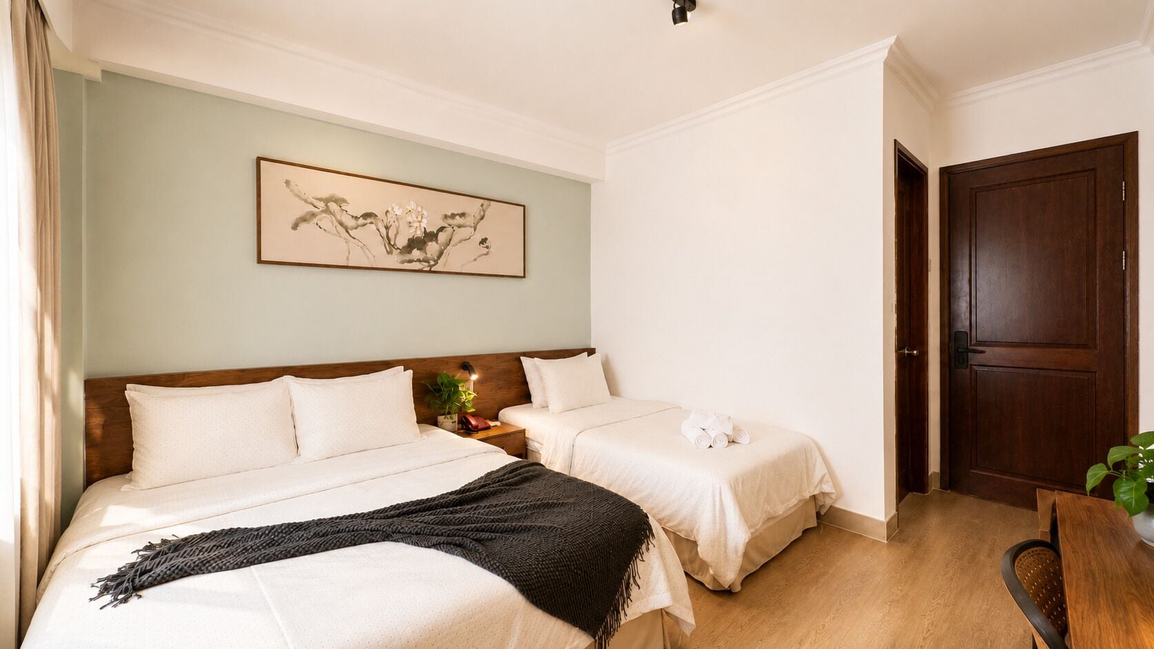 A hotel room with two beds, a wooden headboard, a framed artwork on the wall, and a wooden door.