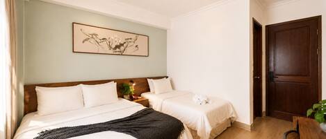 A hotel room with two beds, a wooden headboard, a framed artwork on the wall, and a wooden door.