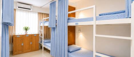 Habitación con literas, un armario de madera, una planta en maceta y una ventana con cortinas.