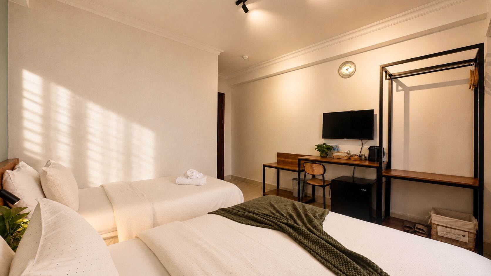 A hotel room with two beds, a desk, a chair, a television, and a large mirror.