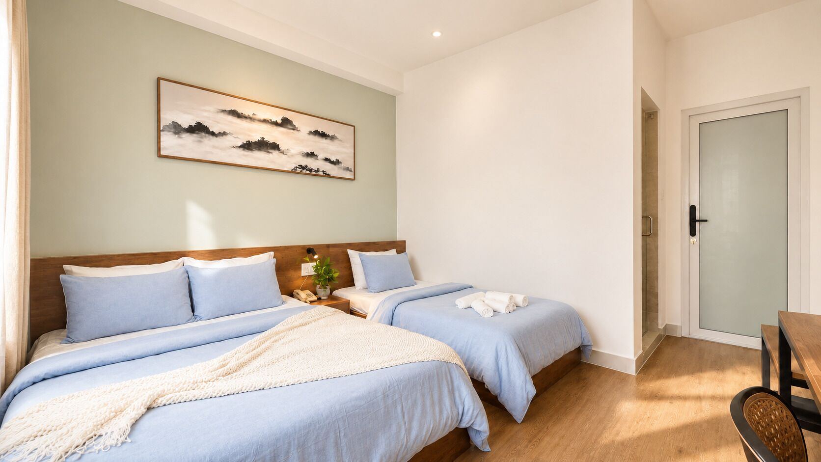 A bedroom with two beds, a bedside table with a lamp, a painting on the wall, and a door with frosted glass.