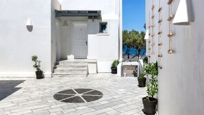 Un edificio blanco con una puerta y escalones que conducen a un acceso cubierto. Hay plantas en macetas y un diseño circular de piedra en el suelo.