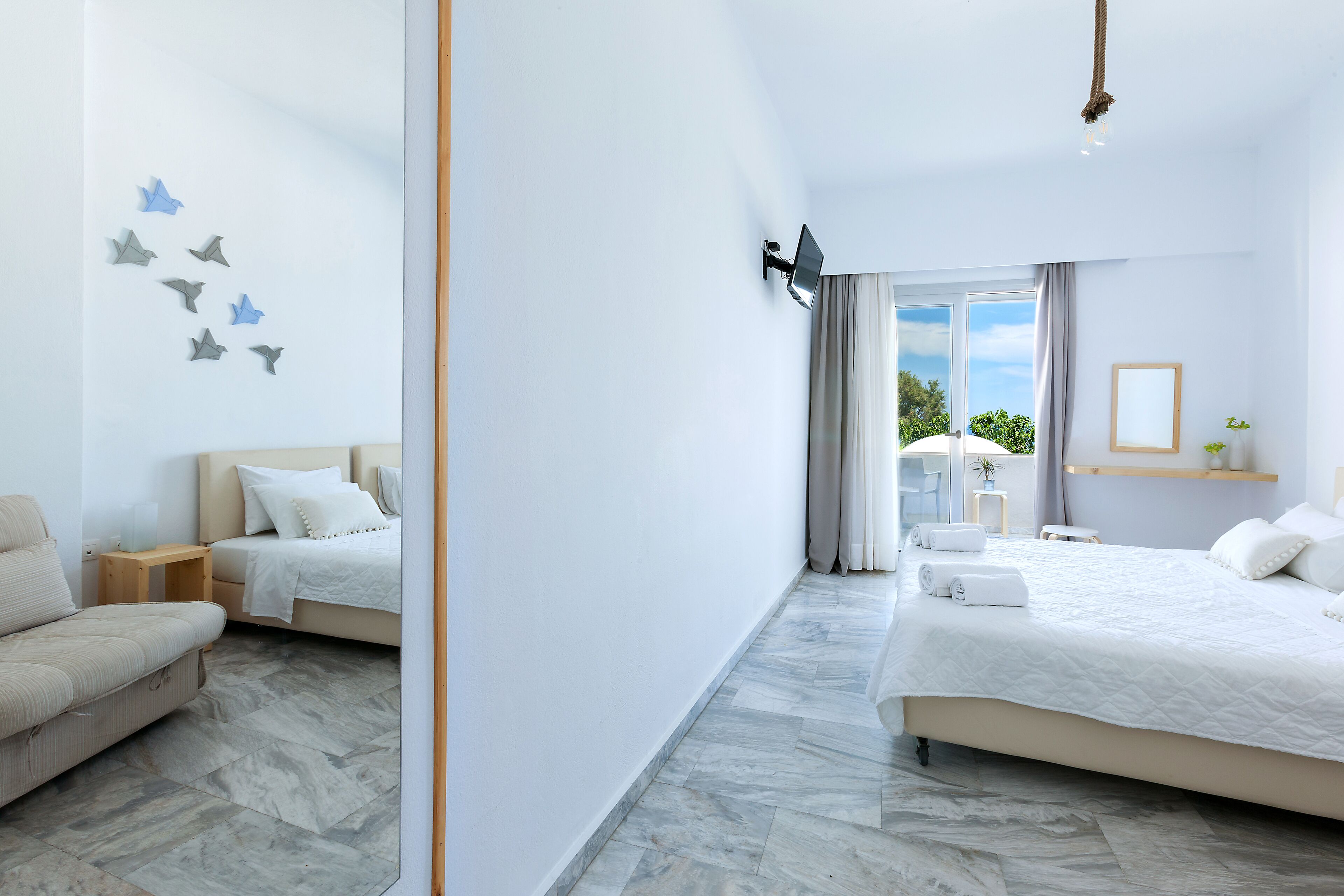 A modern hotel room with two beds, a sofa, a small table, and a mirror.
