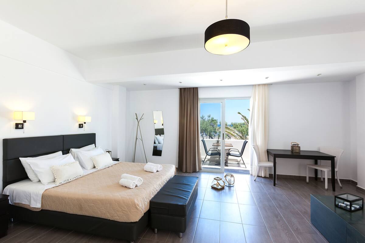 A modern hotel room with a large bed, a desk, and a balcony with a view.