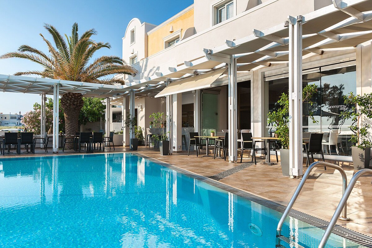 A swimming pool with a pergola, outdoor seating, and palm trees.