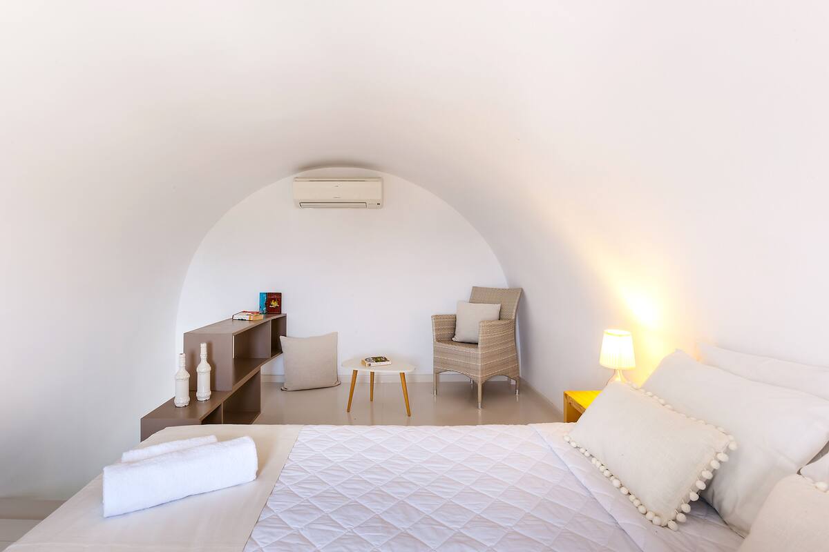 A bedroom with a bed, a chair, a small table, and a lamp.