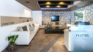 Una sala de estar moderna con una pared de piedra, un televisor de pantalla plana, un sofá blanco y una mesa de centro de vidrio.