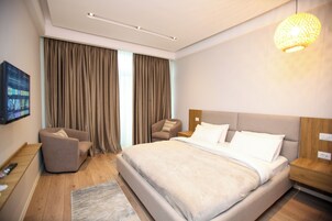Una habitación de hotel moderna con una cama grande, un rincón de descanso con una silla, un televisor montado en la pared y una mesita de noche de madera.