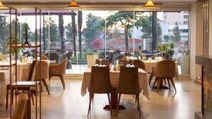 A dining area with tables and chairs, large windows, and indoor plants. - Vlora International  (Vlorë)