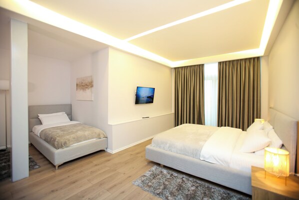A modern hotel room with a large bed, a smaller bed, a flat-screen TV, and a nightstand with a lamp. - Vlora International (Vlorë)