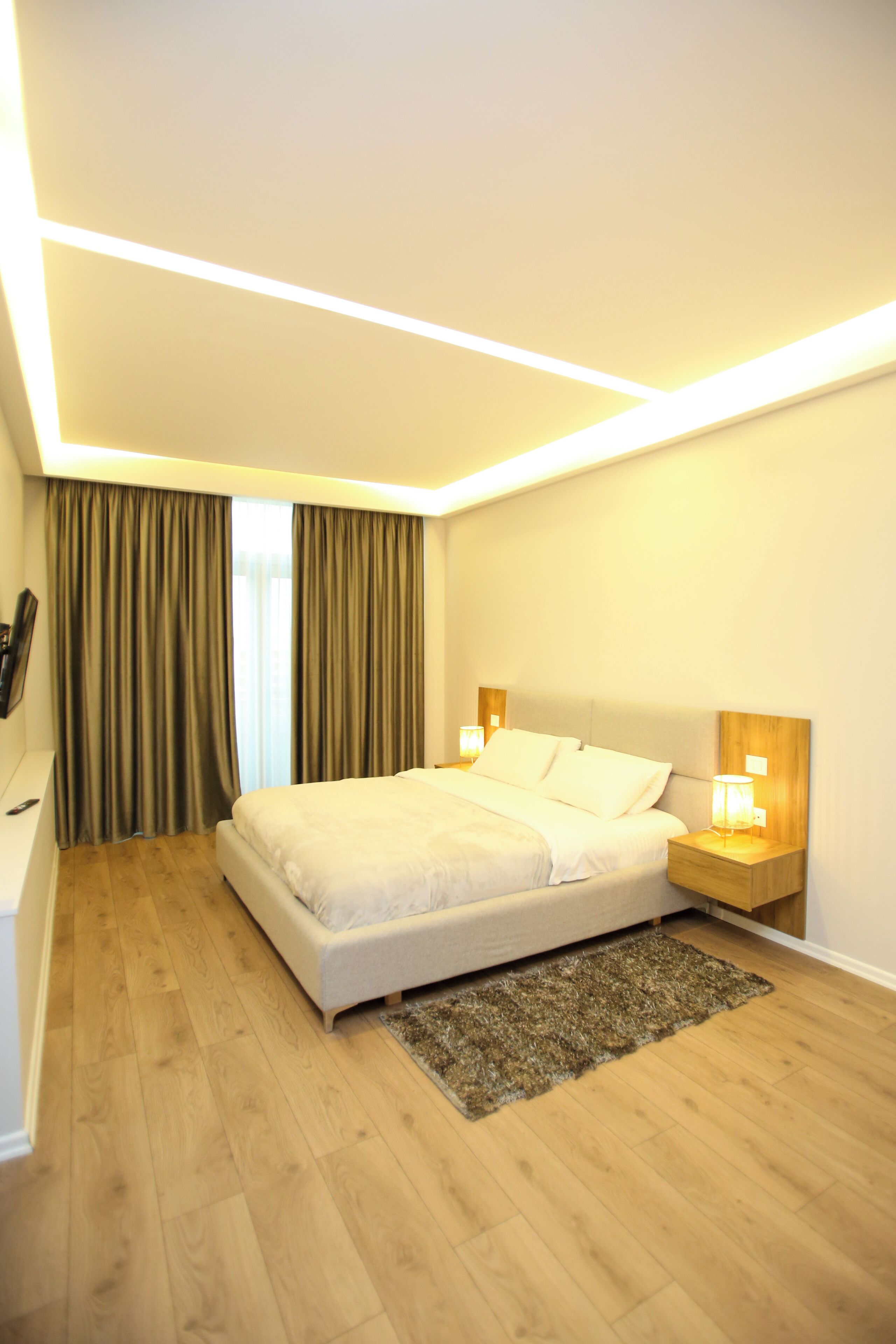 A modern hotel room with a large bed, wooden flooring, a small rug, and two bedside lamps.