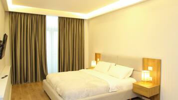 A modern hotel room with a large bed, wooden flooring, a small rug, and two bedside lamps.