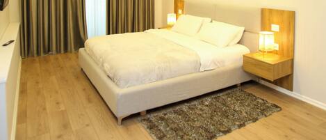 A modern hotel room with a large bed, wooden flooring, a small rug, and two bedside lamps.