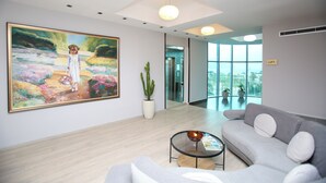 A modern interior with a large floral painting, a grey sofa, a small table, and a potted plant. - Vlora International  (Vlorë)