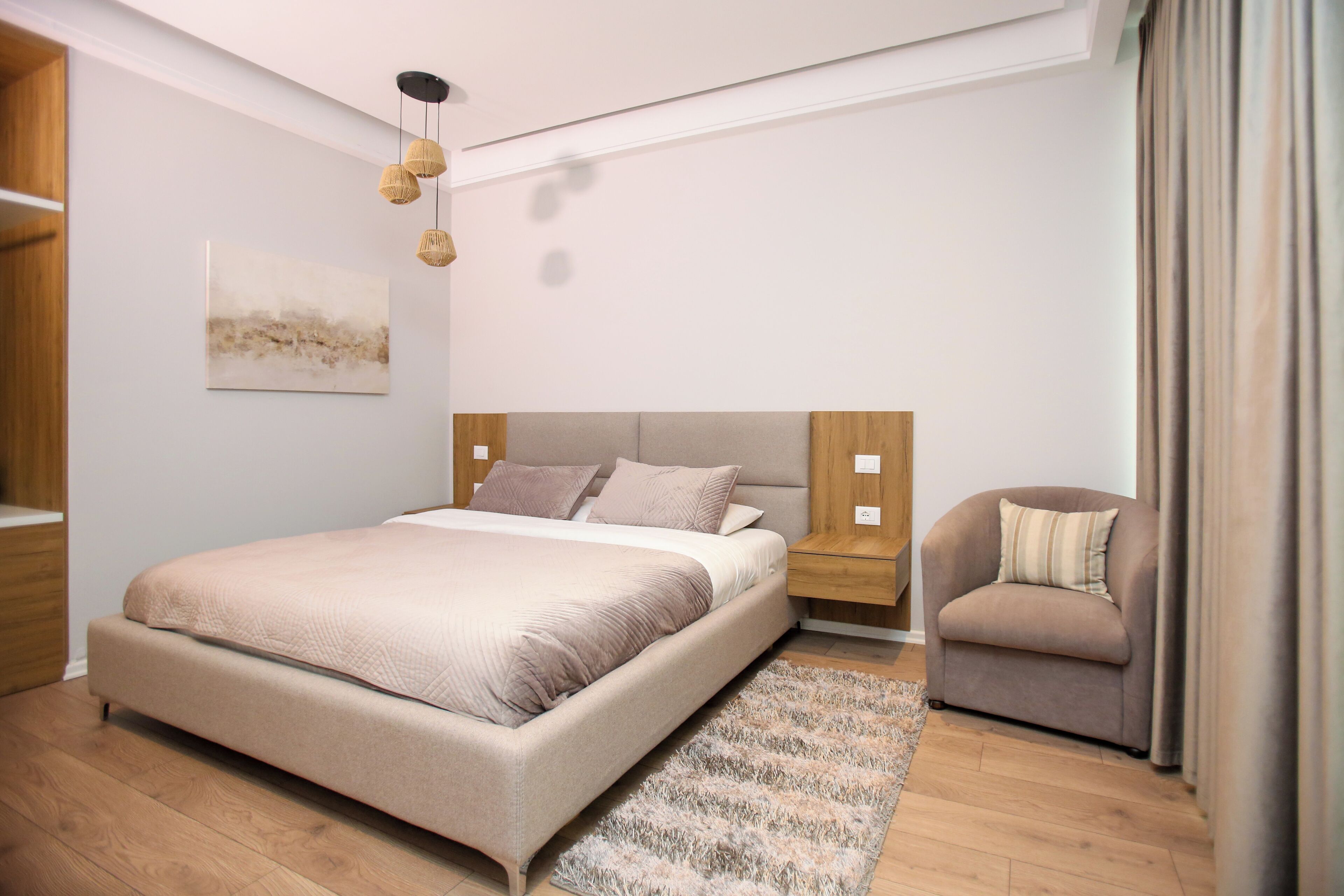 Un dormitorio moderno con una cama grande, una mesita de noche, una silla y una lámpara colgante.