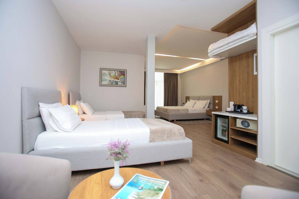 Ett modernt hotellrum med en stor säng, en mindre säng, ett skrivbord och en sittgrupp.