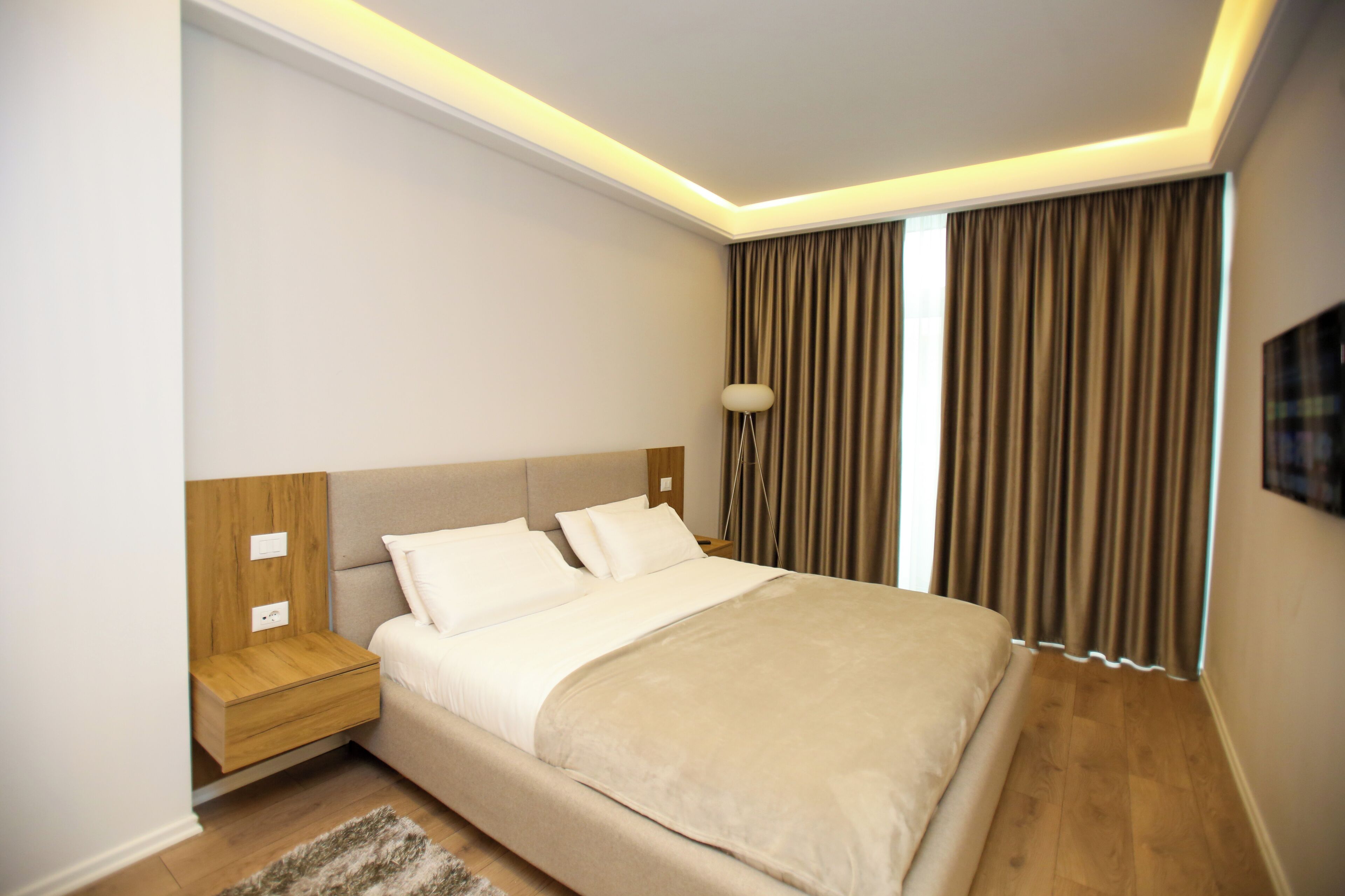 A modern hotel room with a large bed, wooden nightstand, and a lamp.