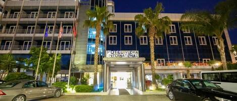 Un hotel moderno con una entrada destacada, varios pisos y palmeras en primer plano.
