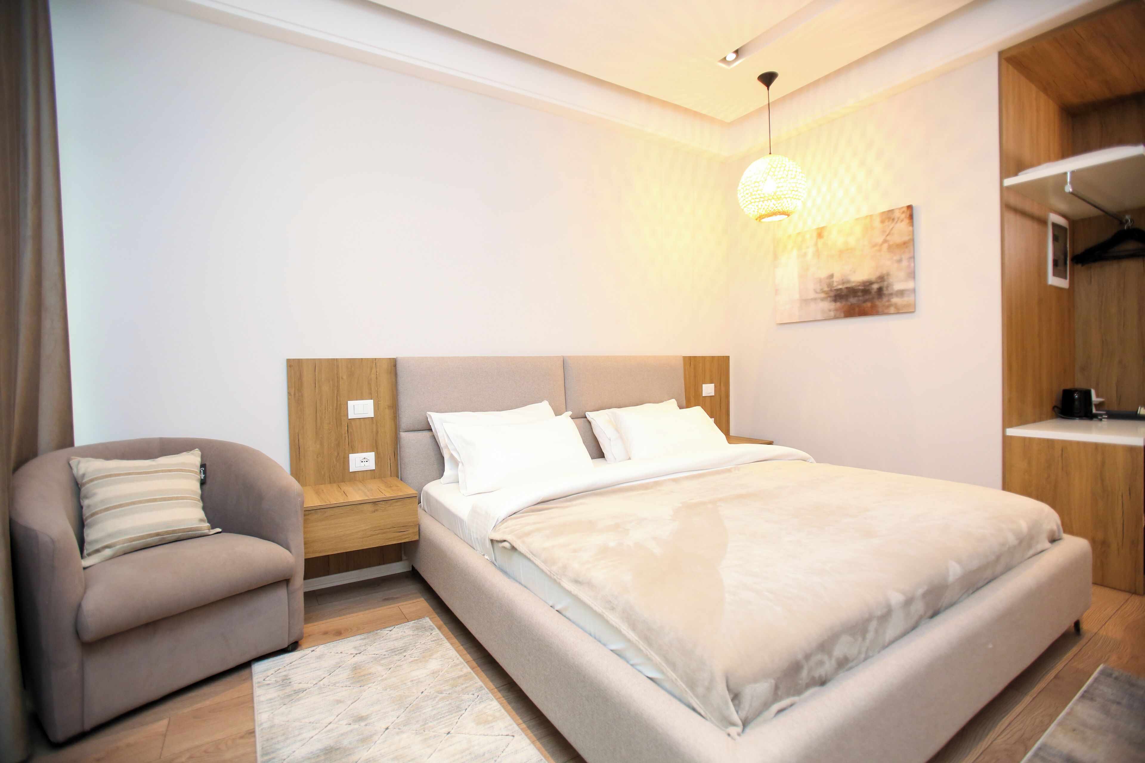 Een moderne slaapkamer met een groot bed, een bank, een nachtkastje en een hanglamp.