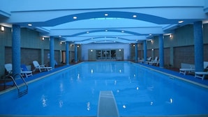 A large indoor swimming pool with lounge chairs and a high ceiling. - Vlora International  (Vlorë)