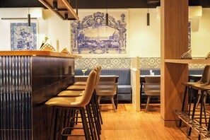 Zona de bar con taburetes, una barra de madera y una pared decorada detrás.