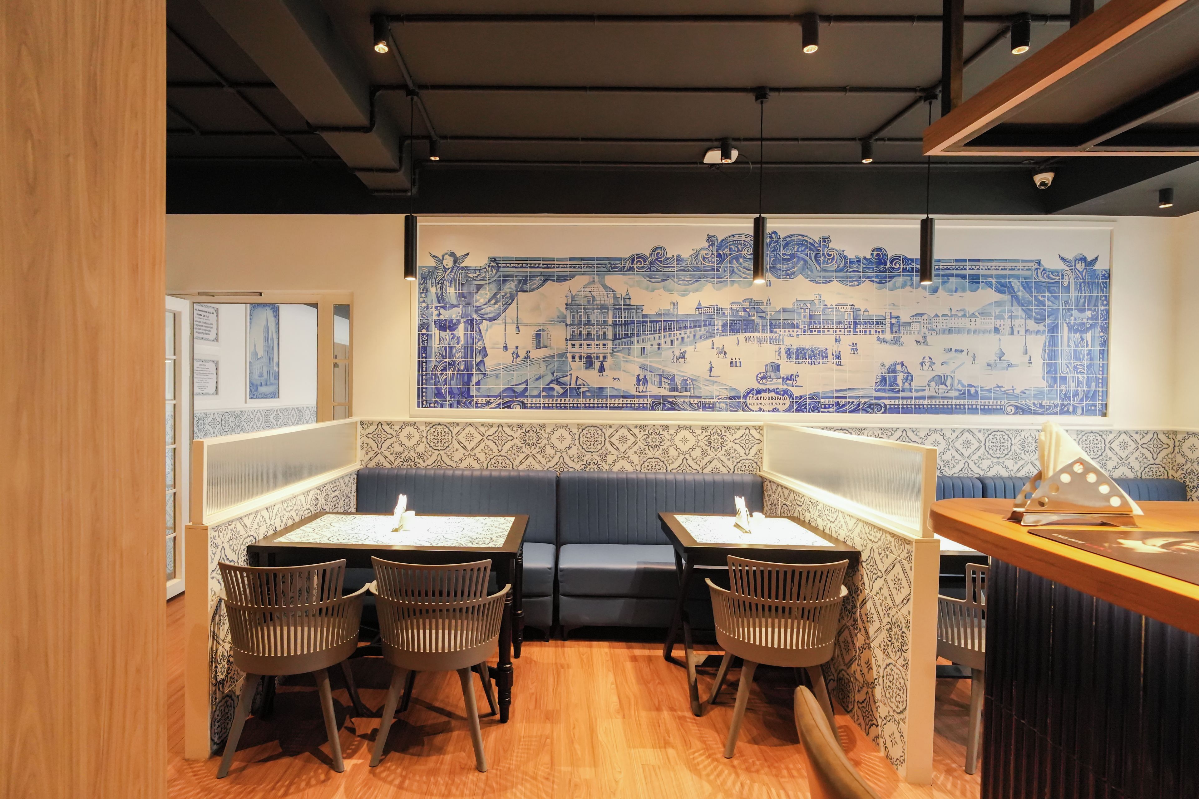 A restaurant interior with a blue and white patterned wall mural, wooden flooring, and a seating area with tables and chairs.