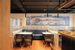 Interior de un restaurante con un mural azul y blanco, suelo de madera y una zona de estar con mesas y sillas.