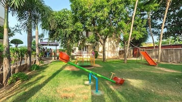 A playground with seesaws, slides, and a small building in the background.