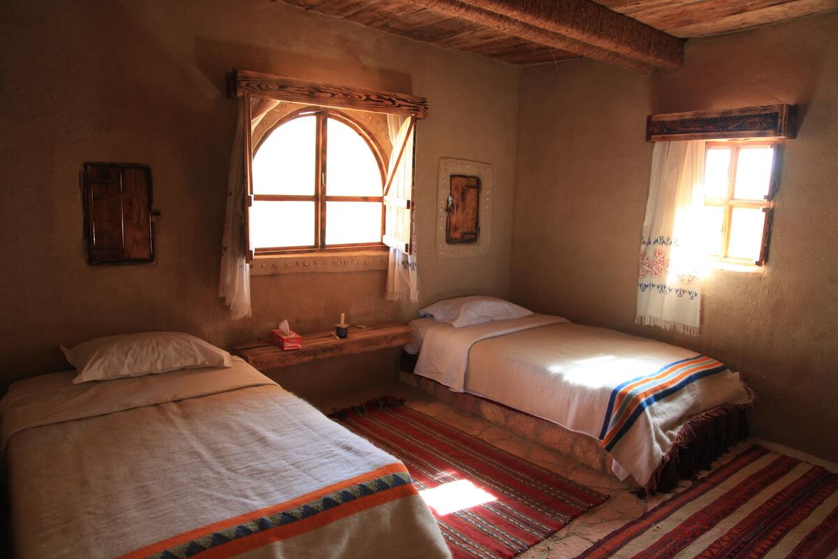Ein Zimmer mit zwei Betten, einem Vorhangfenster, einem Holzkopfende und einer Steinwand.