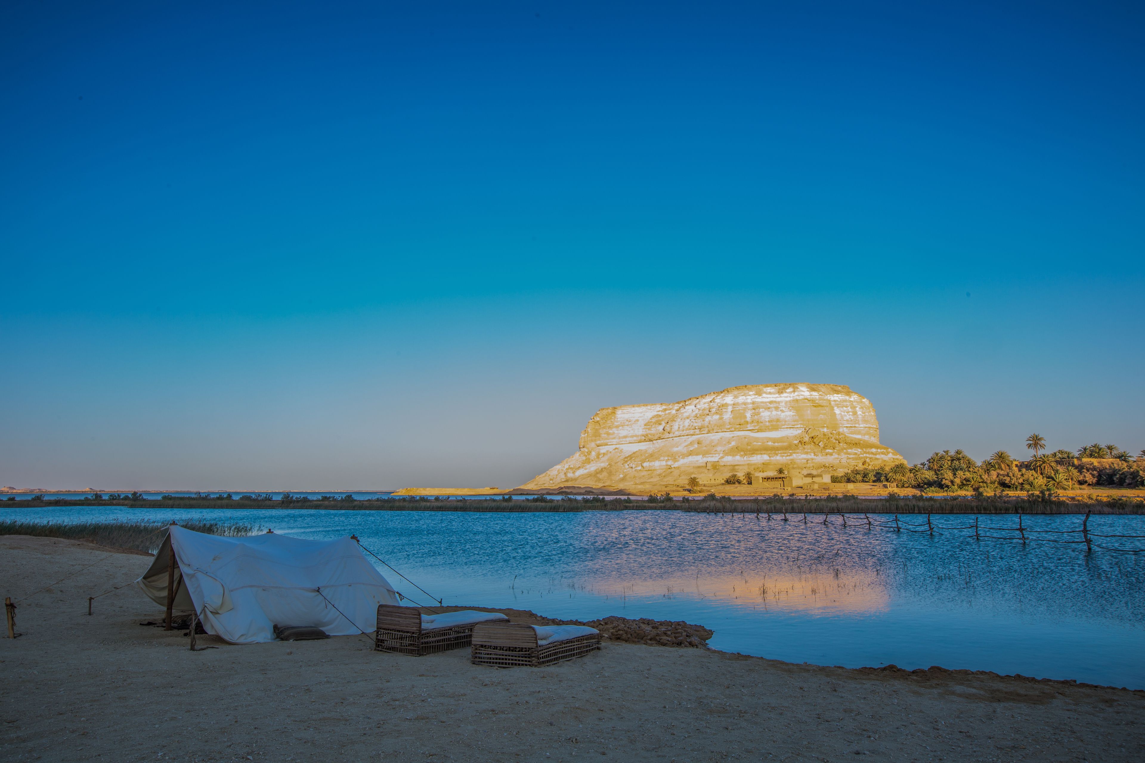 A tent set up near a body of water with a large rock formation in the background.