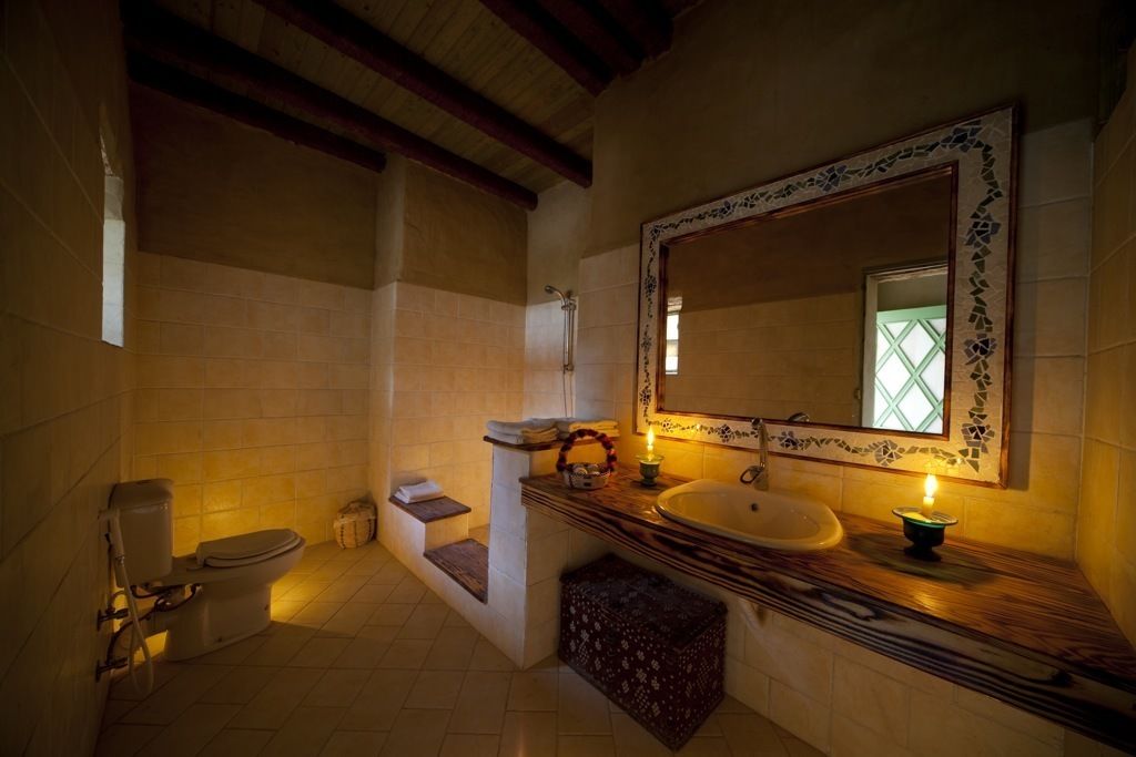 A bathroom with a large mirror, a sink, and a toilet. There is a small bench and a candle on the counter.