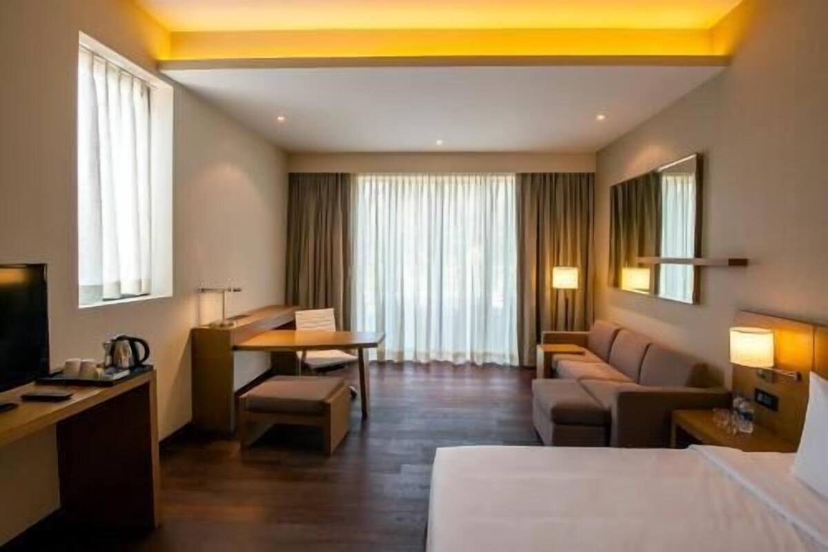 A hotel room with a bed, a desk, a chair, a sofa, and a TV.