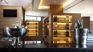 Un espace bar moderne avec un grand récipient métallique, des bouteilles de vin et des verres disposés sur des étagères.