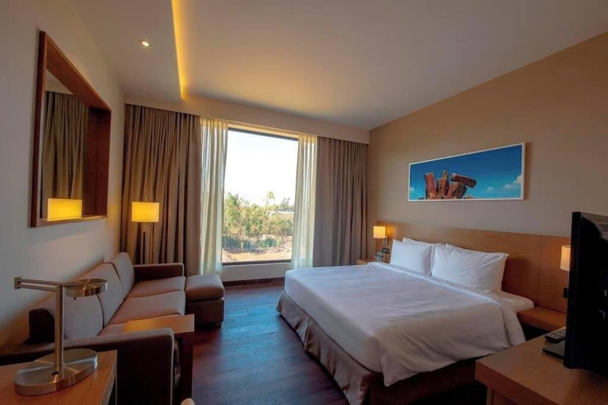 A hotel room with a bed, a desk, a chair, a TV, and a window with curtains.
