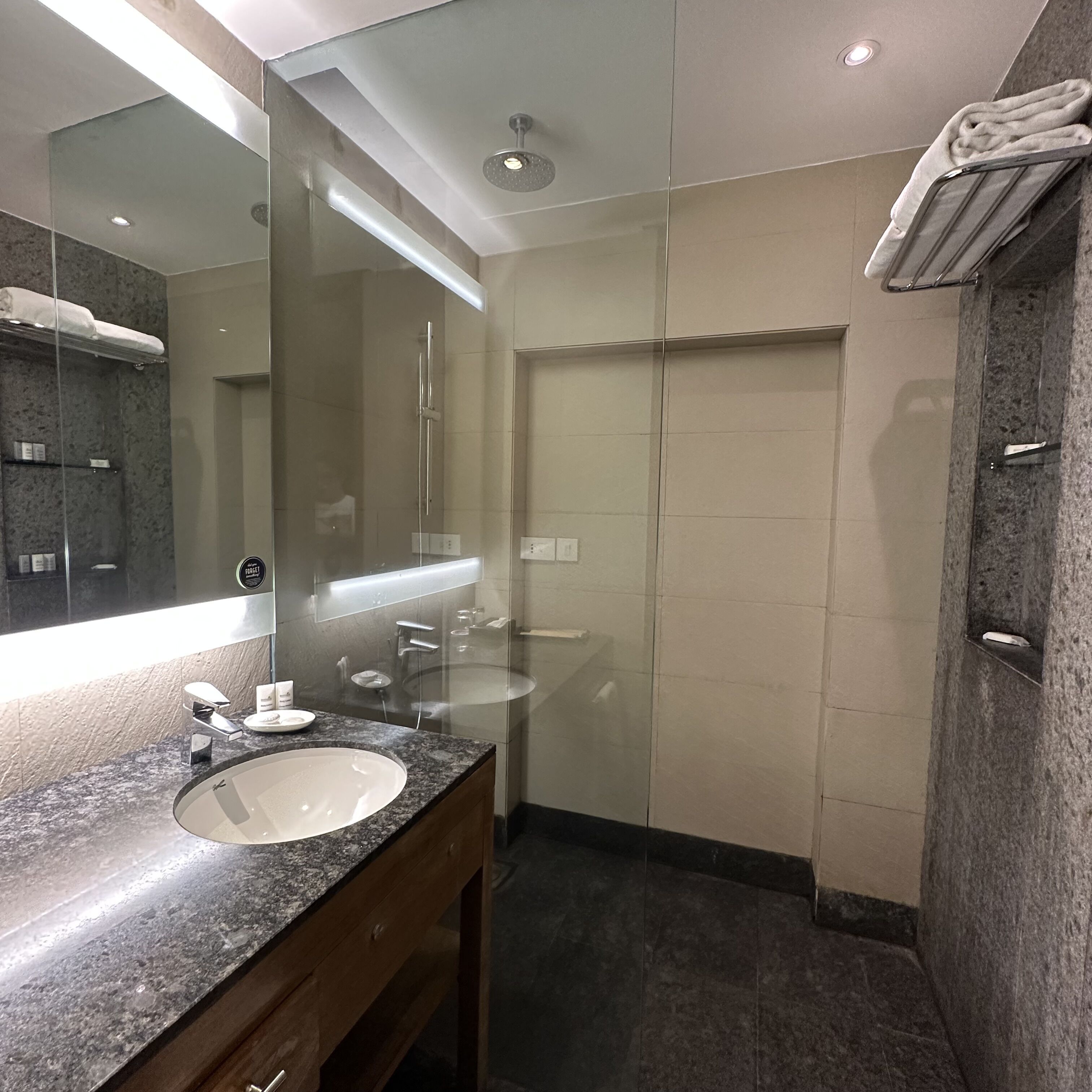Un baño moderno con lavamanos de encimera de granito, un espejo grande, ducha con mampara de vidrio y un perchero para toallas.