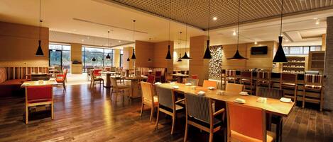 A spacious restaurant with wooden flooring, multiple dining tables, and chairs.