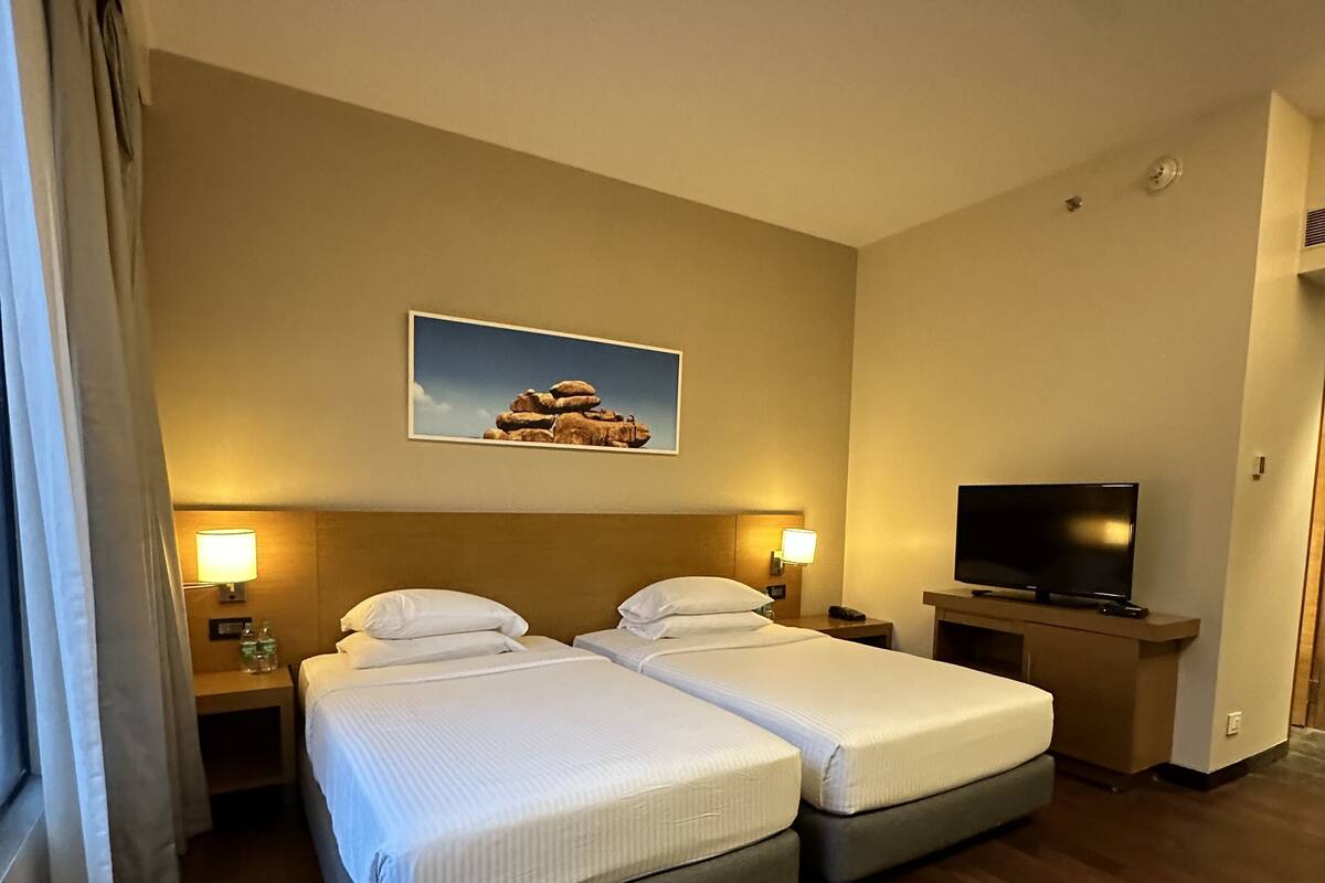 A hotel room with two beds, a television, and a painting on the wall.