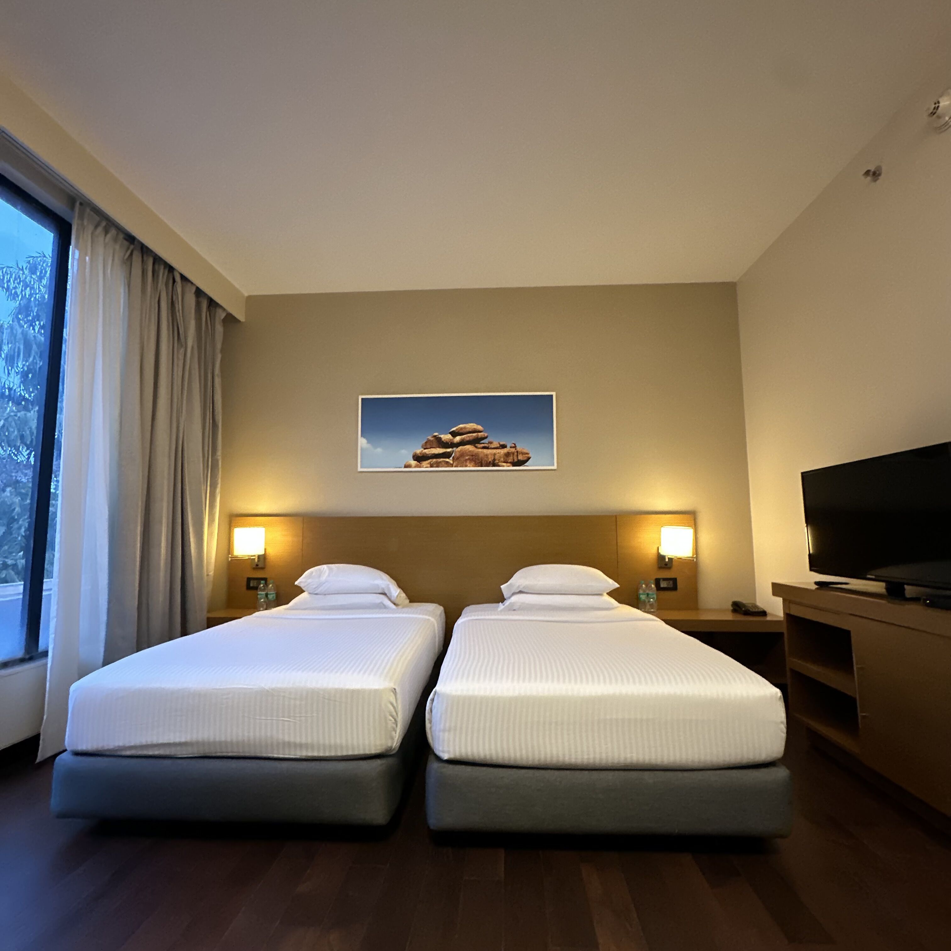 A hotel room with two beds, a television, and a painting on the wall.
