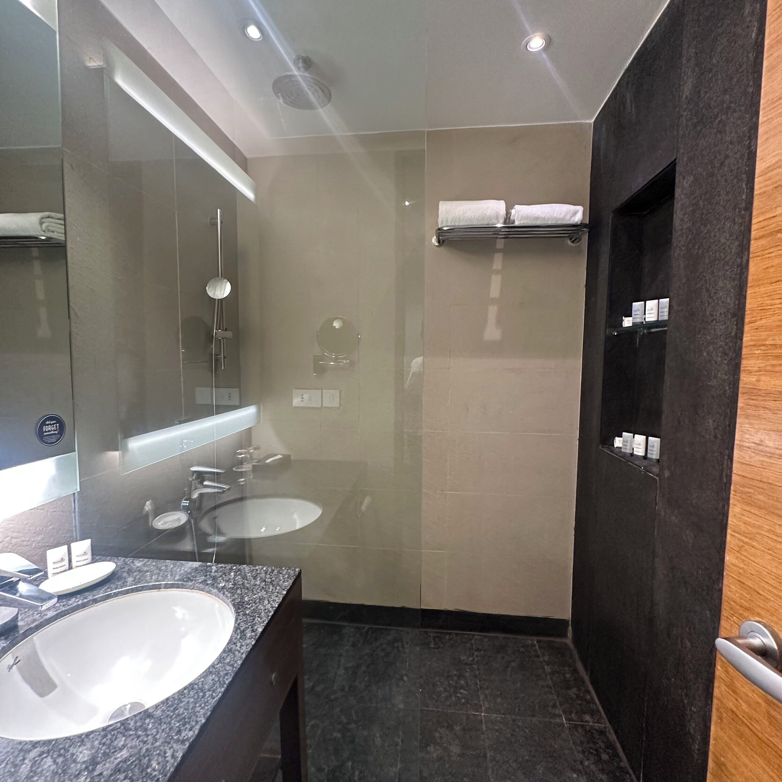 Un baño moderno con dos lavamanos, una ducha con mampara de cristal y una puerta de madera.
