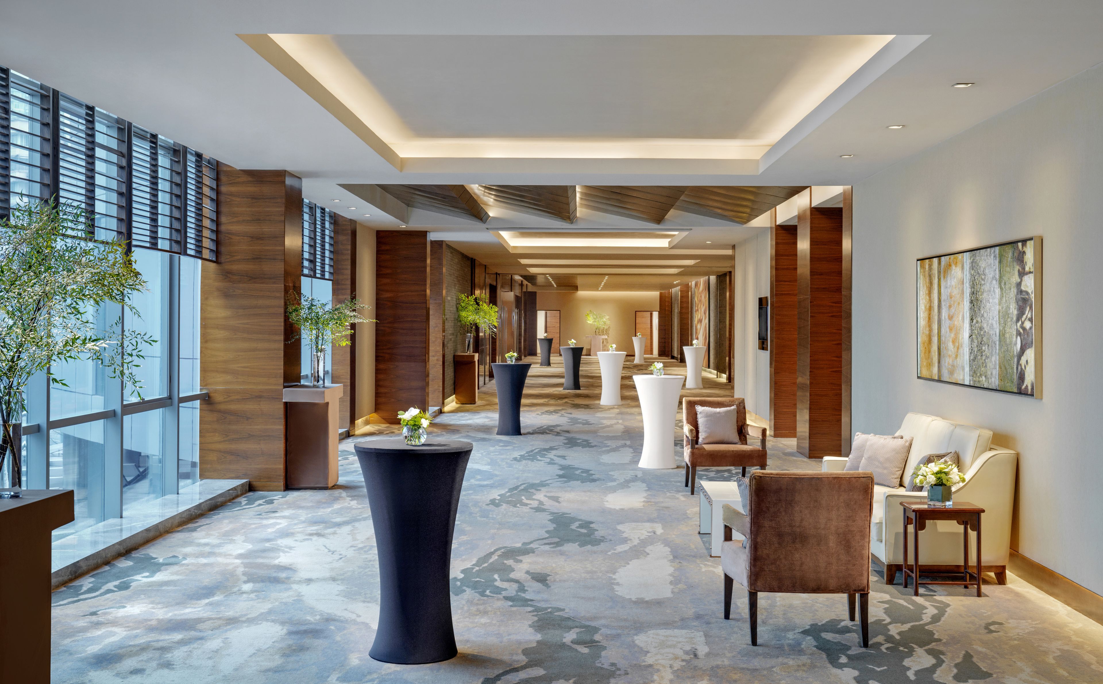 A modern hotel lobby with a central column, seating areas, and a large window on the left.