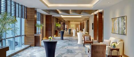 A modern hotel lobby with a central column, seating areas, and a large window on the left.