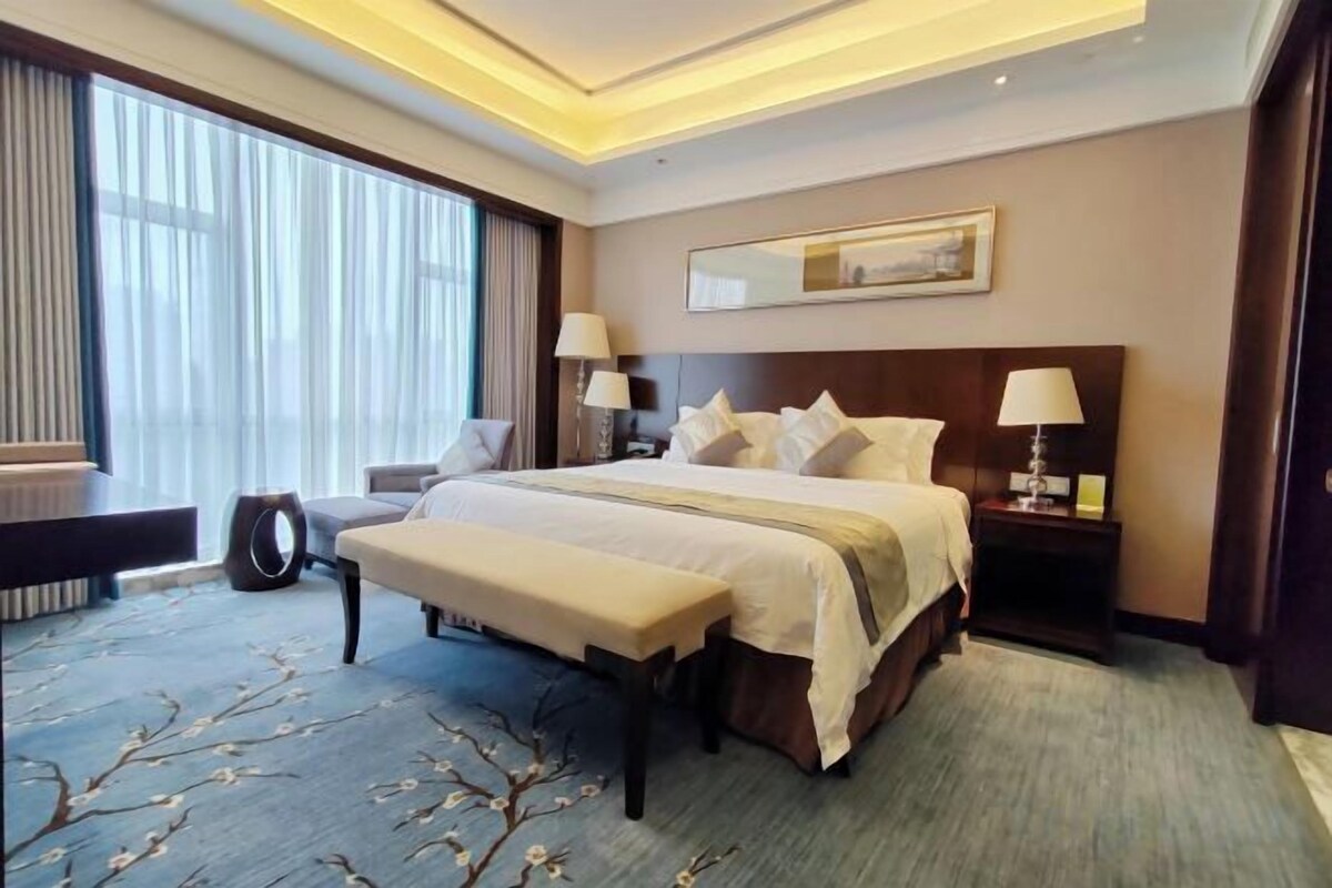 A hotel room with a large bed, bedside tables, a desk, and a view of the outdoors.