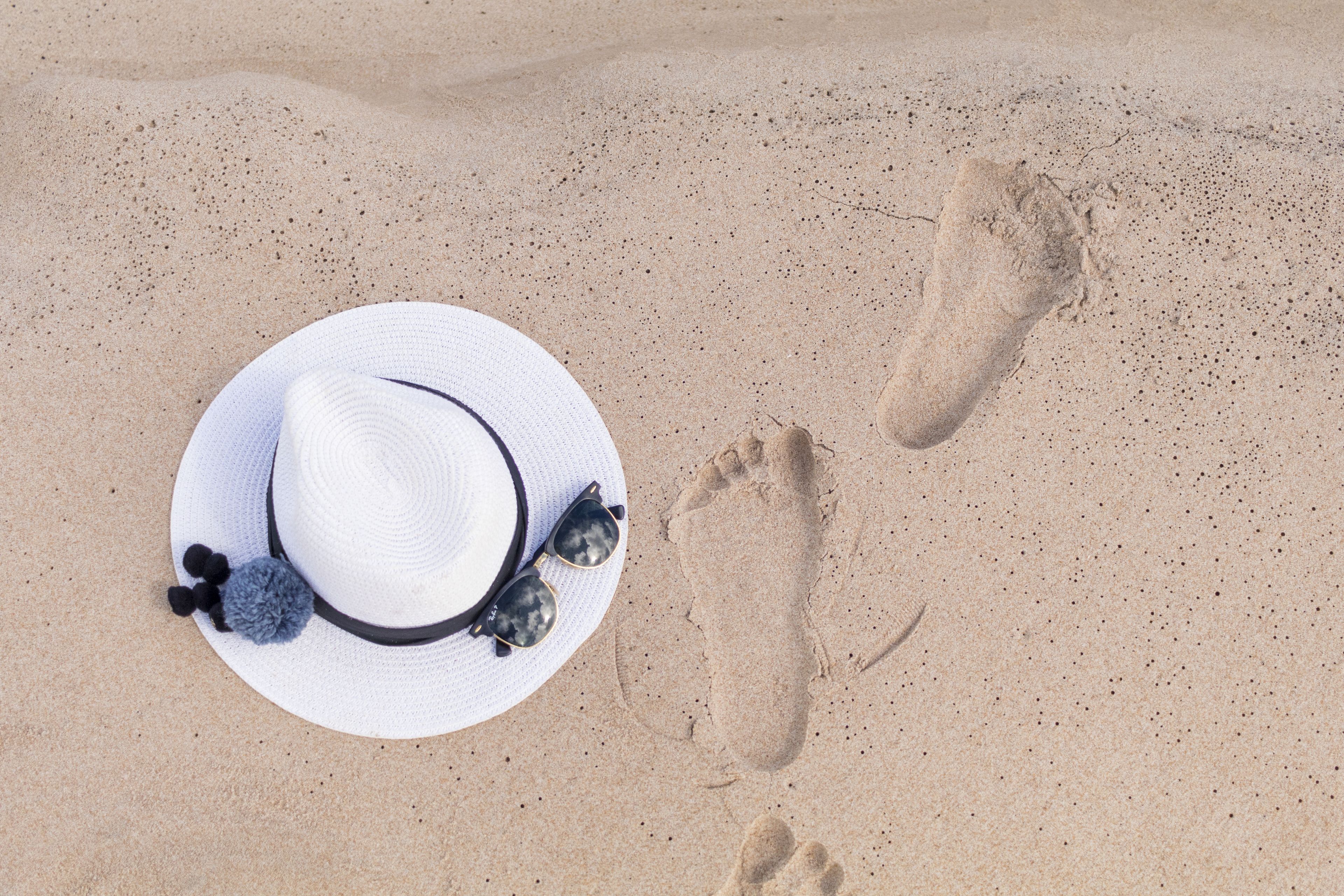 Un cappello bianco con occhiali da sole e un pon pon su una superficie sabbiosa.