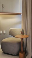 Una habitación moderna con una butaca tapizada de gris, una mesita de madera con una escultura de un pájaro y un estante de madera encima.