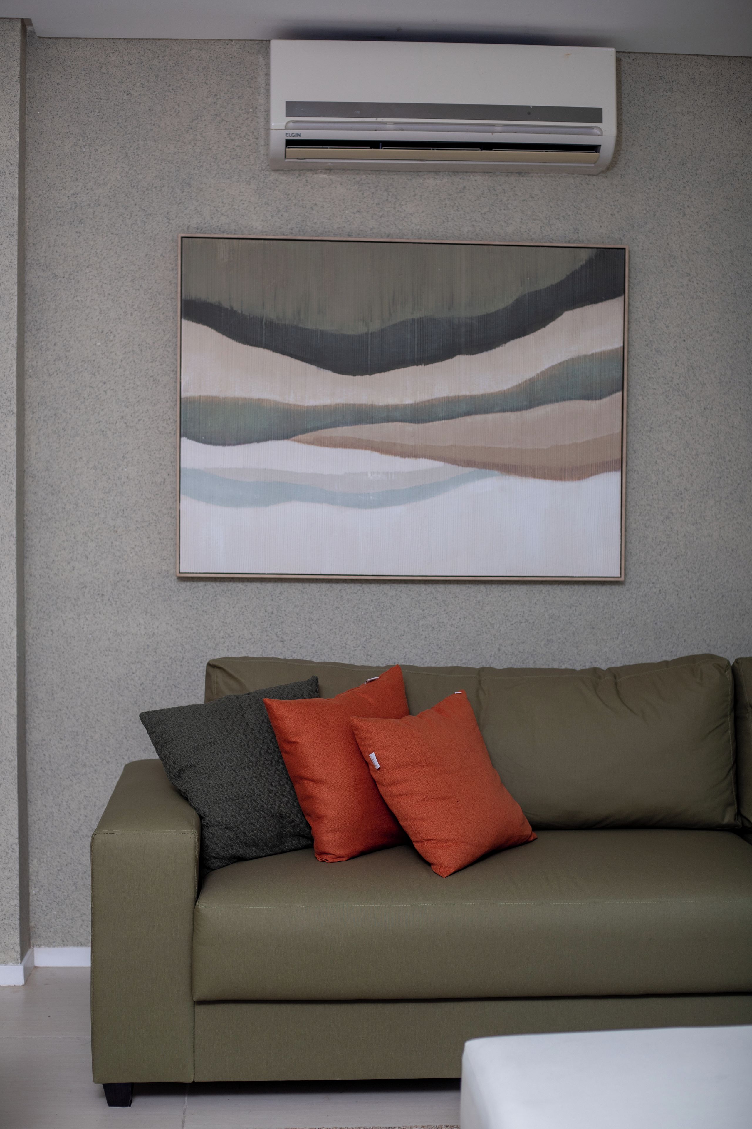 A living room with a green sofa, a wall-mounted air conditioner, and a large abstract painting.